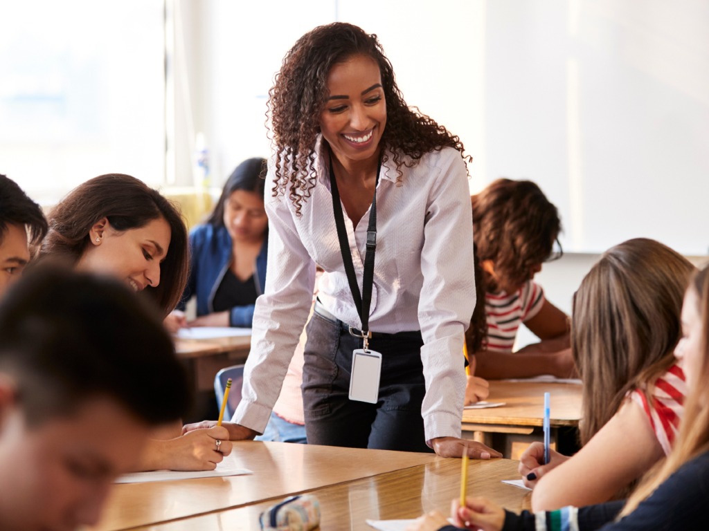 Femme appuyée contre le bureau de la classe regardant les étudiants